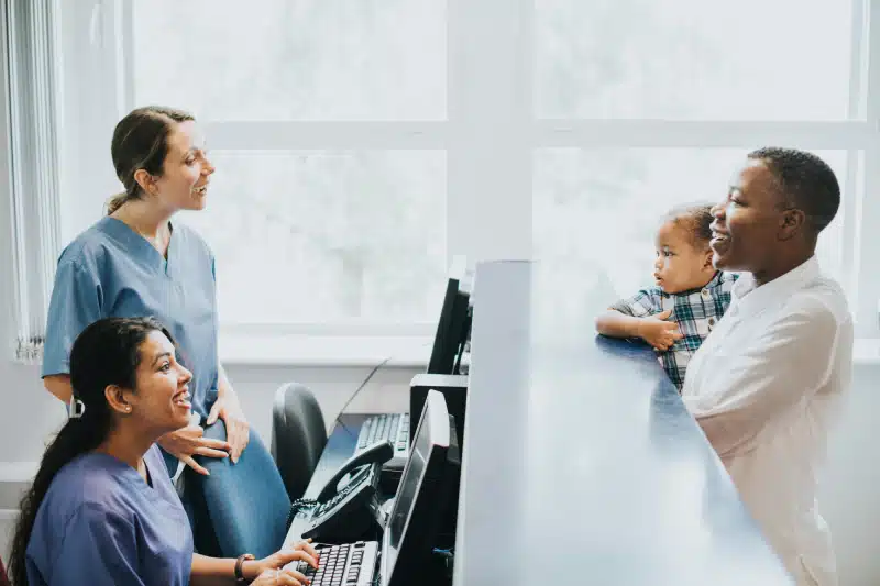 Man with baby talking to nurses at reception