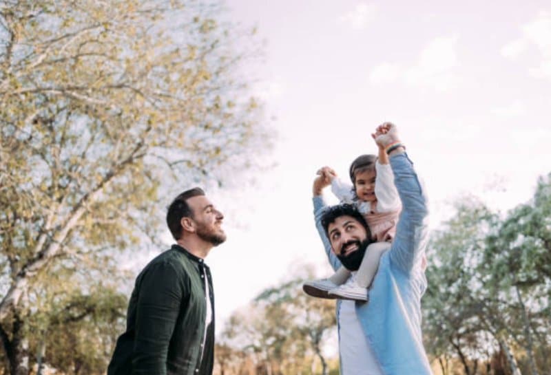 Two men in park with young girl on shoulders