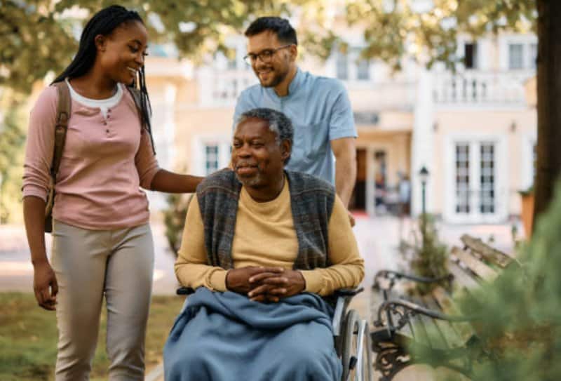 Elderly man sitting in wheelchair with young woman and carer